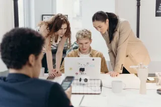 Three colleagues collaborate on a laptop, embodying teamwork and creativity in a modern office environment.