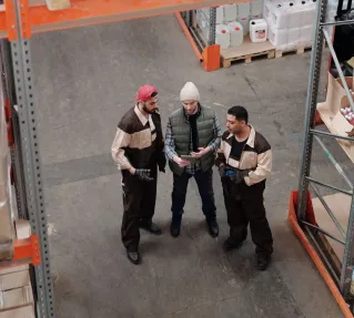 Three warehouse workers discuss logistics in an industrial storage facility.