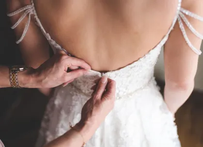 Close-up of hands adjusting a bride's dress, showcasing delicate details and elegance.