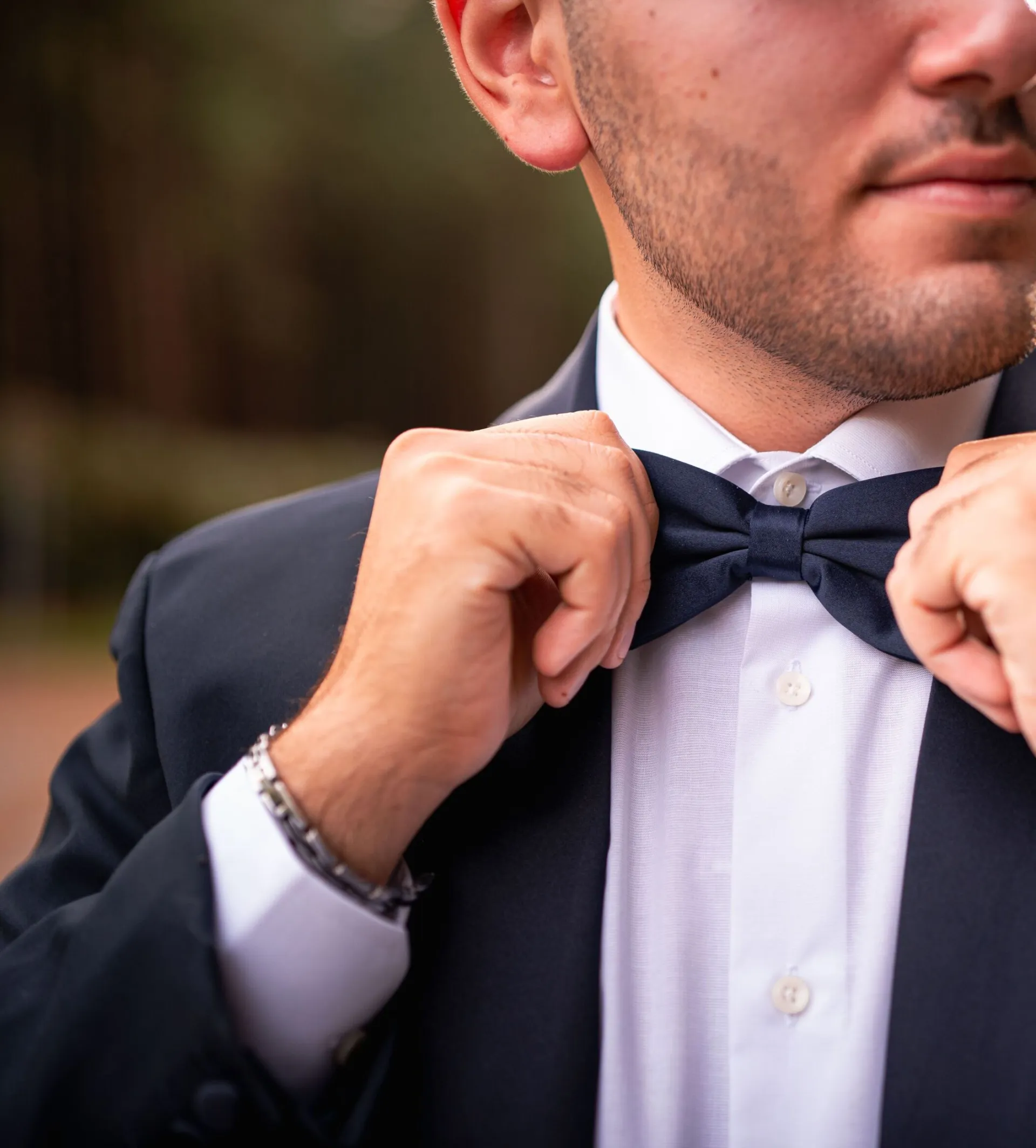 Close-up of a man adjusting a bow tie, showcasing elegance and fashion in an outdoor setting.