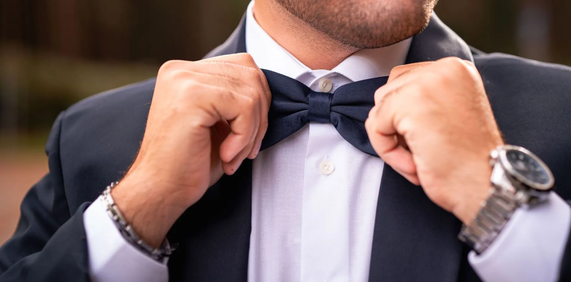 Close-up of a man adjusting a bow tie, showcasing elegance and fashion in an outdoor setting.