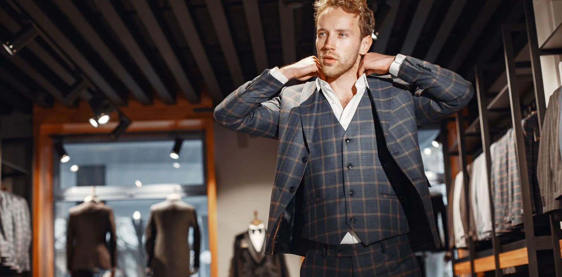 Confident man in a plaid suit adjusts his collar in a stylish boutique.