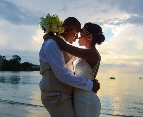 A loving couple embraces on the beach at sunset, celebrating their wedding by the sea.