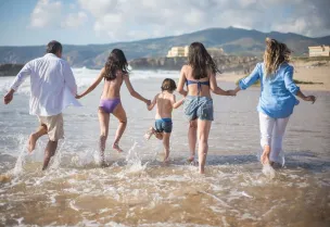 A family having fun running into the ocean on a sunny beach day in Portugal. Joyful and carefree moments.