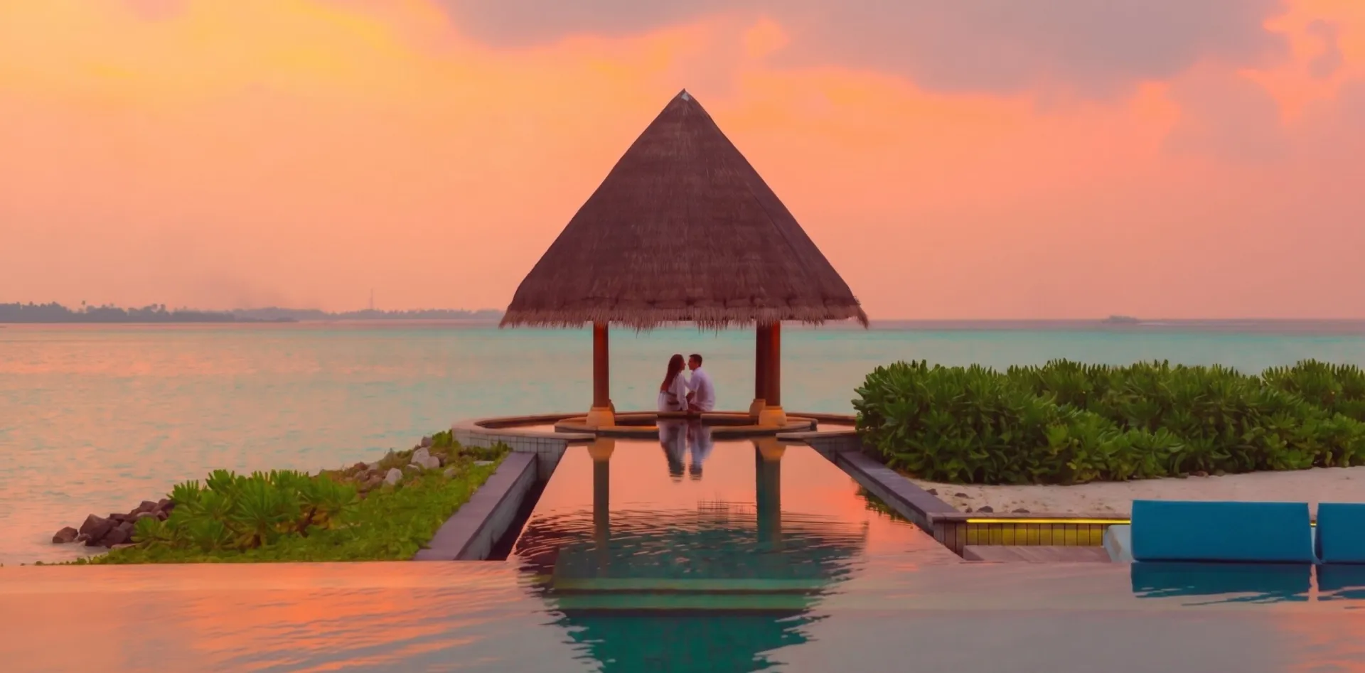 A couple enjoying a romantic moment by the sea and pool under a beach cabana during sunset.