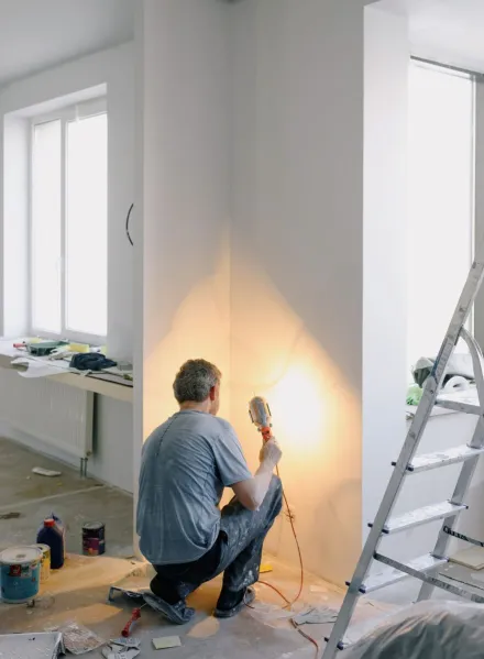 Back view of anonymous male in dirty clothes renovating walls in home while holding lamp