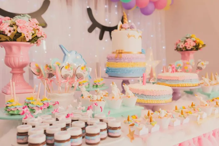 A vibrant unicorn-themed birthday party setup with cakes, cupcakes, and decorations.
