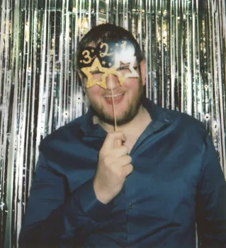 Man celebrating with '30' prop in front of shimmering backdrop, holding a playful expression.