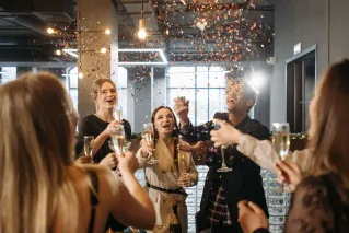 A group of friends celebrates indoors with champagne and confetti in a festive atmosphere.