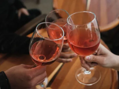 Three friends toasting with rosé wine glasses over a wooden table indoors.
