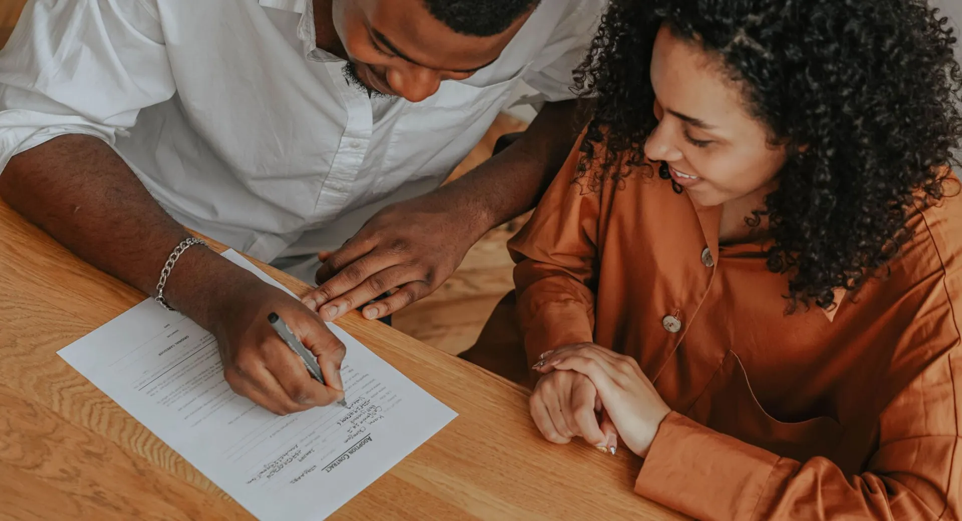 A couple signing an adoption certificate at a table, viewed from above.