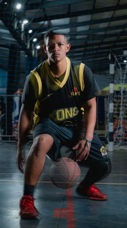 Young male basketball player in uniform posed with a ball on an indoor court.