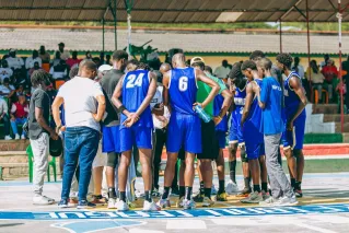 A basketball team strategizes in a huddle during an outdoor game with spectators.