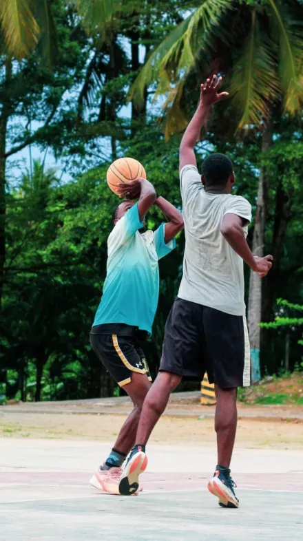 Two men playing an intense basketball game on an outdoor court surrounded by lush greenery.