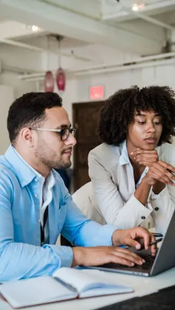 A man and a woman collaborating on a laptop in a modern office setting.