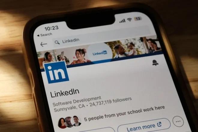 Close-up of a smartphone showing a LinkedIn profile page on a wooden table with shadows.
