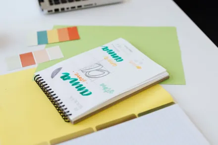 Close-up of colorful design sketches in a spiral notebook with color swatches on a white desk.