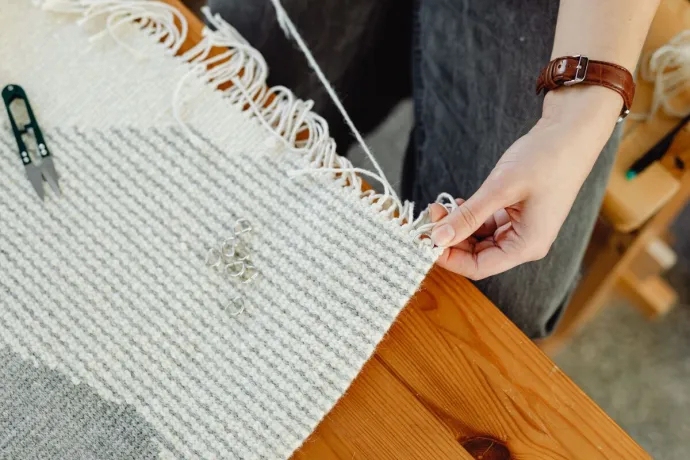 Close-up of a person weaving fabric on a wooden loom, showcasing craftsmanship and detail.