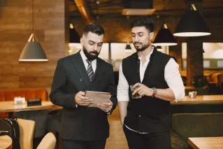 Two businessmen in a cafe discussing work using a tablet and enjoying a drink.