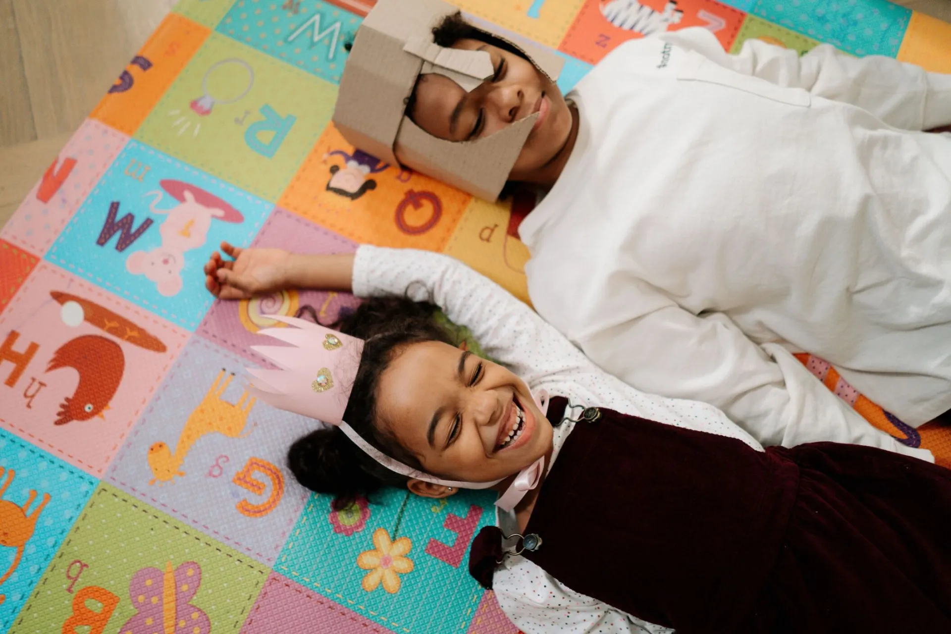 Two children having fun on a colorful play mat indoors, wearing creative DIY costumes.