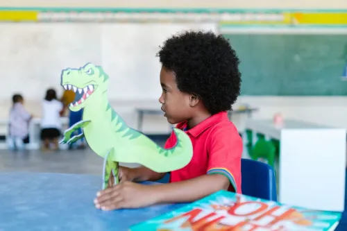 Young boy in a classroom playing with a dinosaur toy, highlighting learning fun.