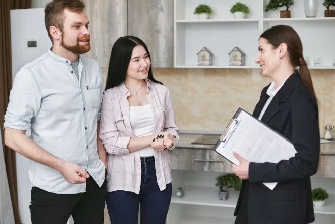 A young couple engaging in a conversation with a real estate agent inside a modern kitchen setting.