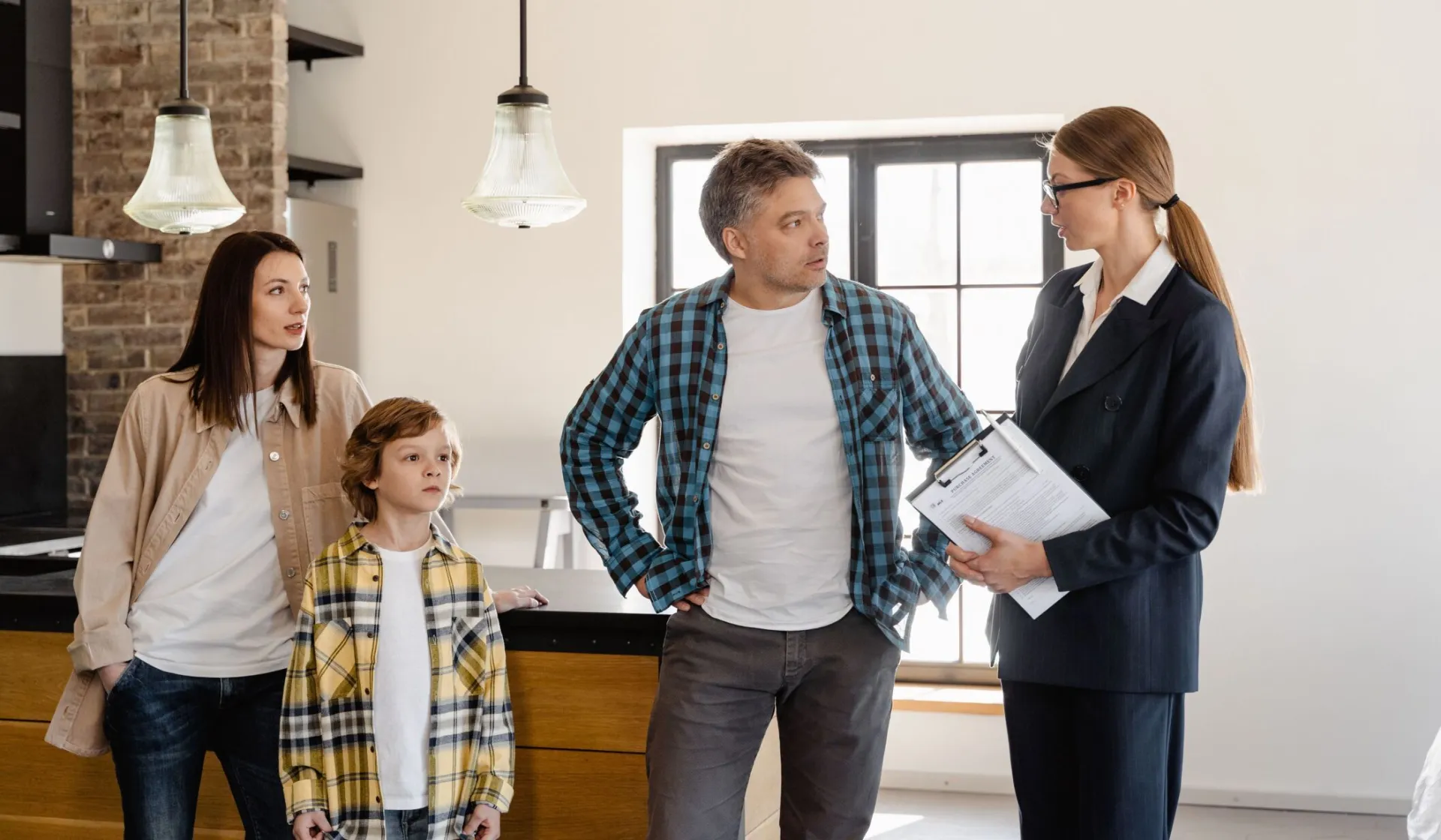 Family with child talks to real estate agent in modern kitchen during home showing.