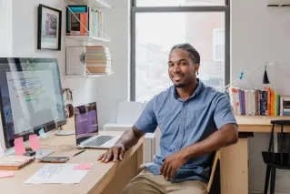 Confident professional man with a welcoming smile sitting at a desk in a contemporary office setting.