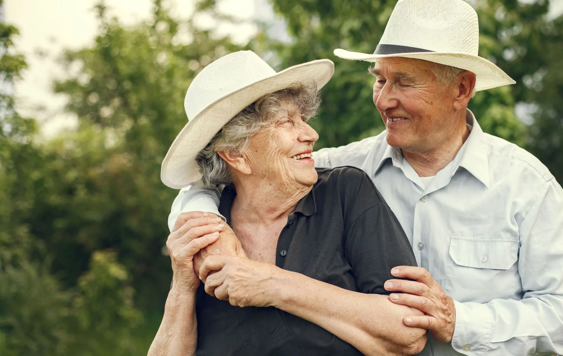 Happy senior couple wearing hats, sharing a joyful moment outdoors, embracing and smiling.