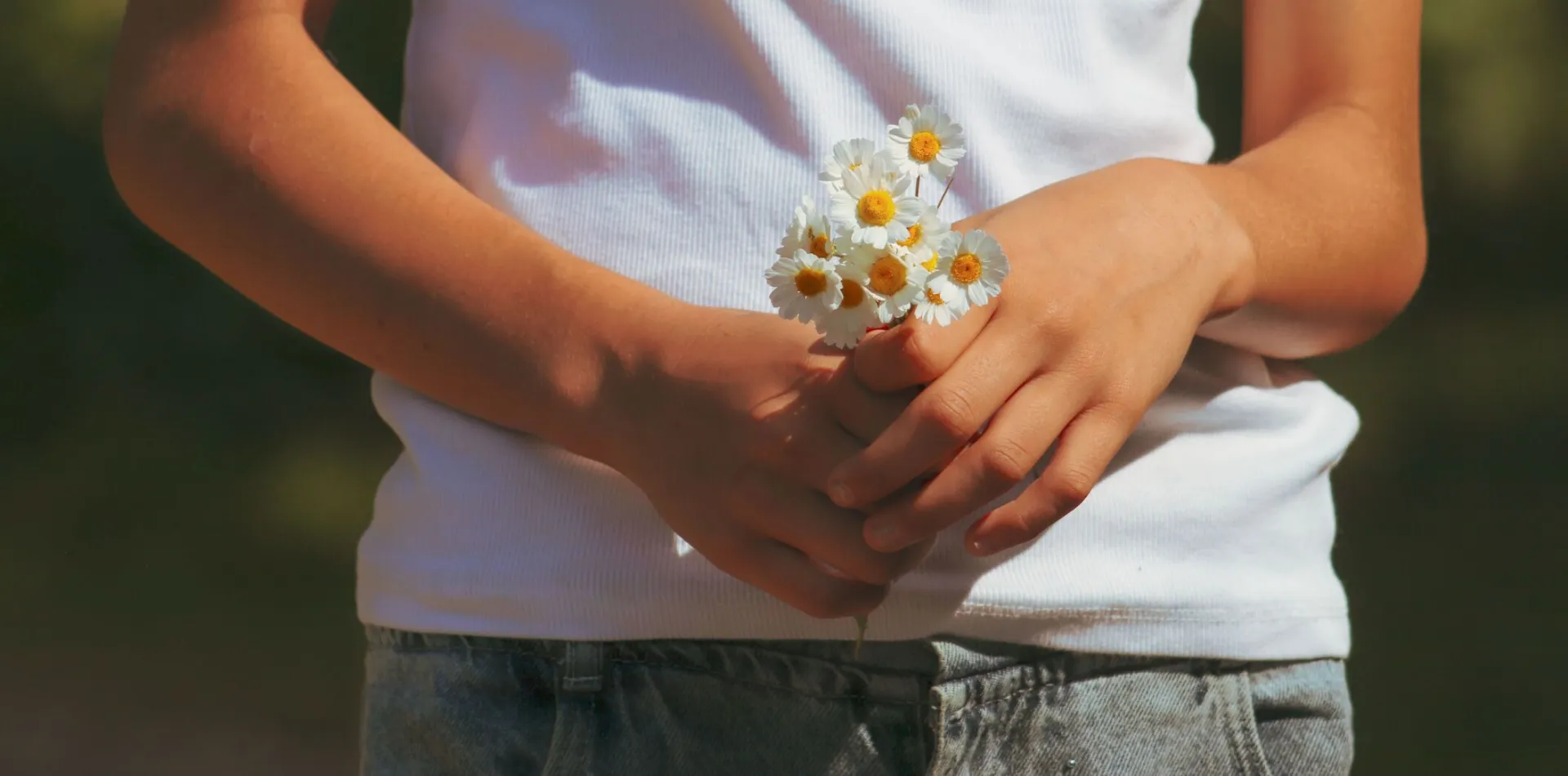 A person in casual clothing holds a small bunch of daisies outdoors on a sunny day, creating a serene and natural mood.