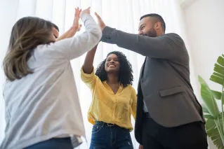 A group of diverse colleagues celebrating teamwork indoors with joyful high fives.