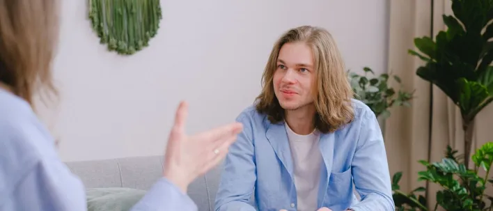 Young man with long hair in a therapy session, actively engaged in conversation.