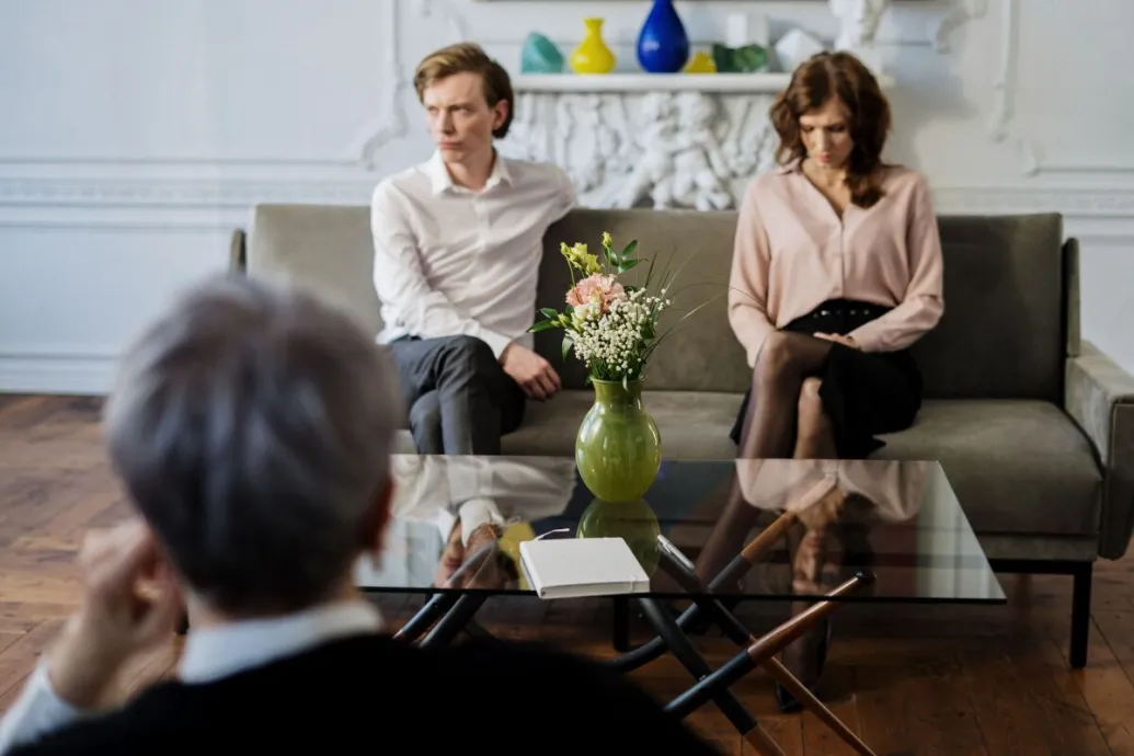 A couple sits on a sofa during a therapy session with a counselor, focusing on relationship issues.