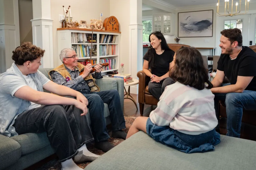 A joyful multigenerational family gathering in a cozy living room, sharing stories and playing a violin.