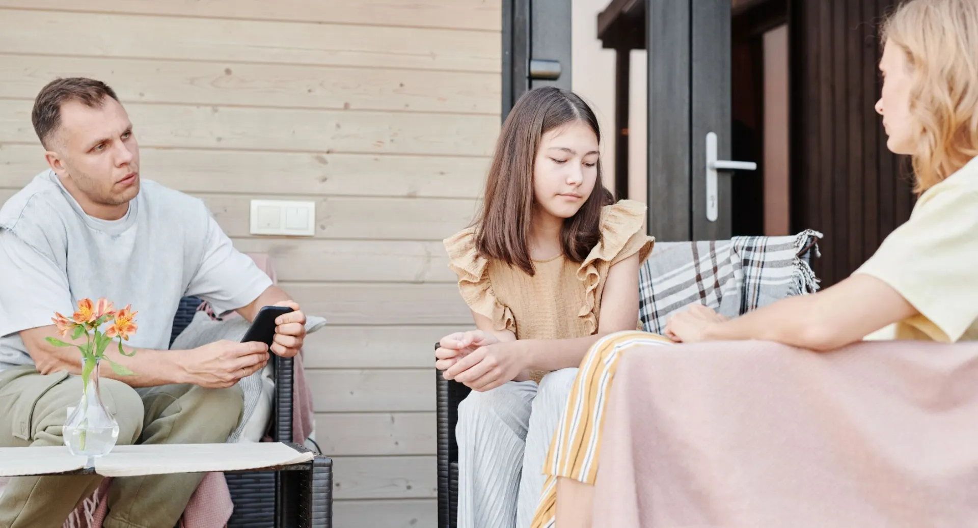 A family of three having a serious conversation outdoors on a patio.