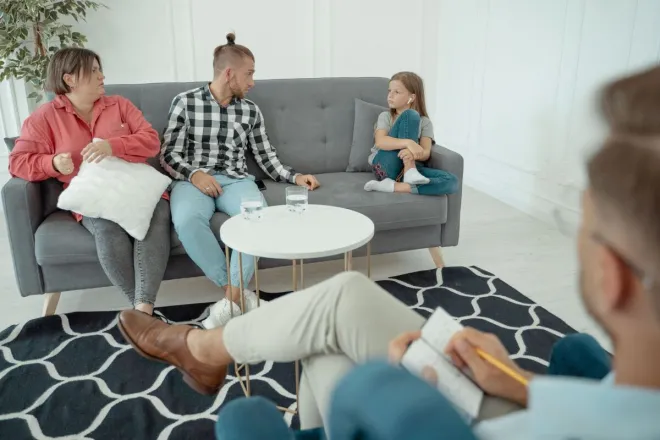 Family therapy session featuring parents and child with therapist in a cozy office setting.