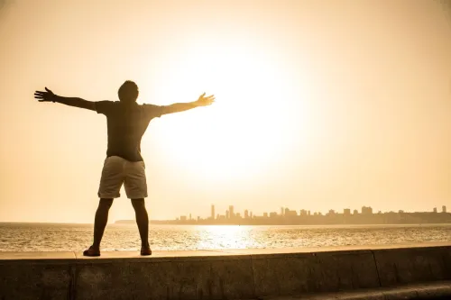 Man stands with arms outstretched facing the sunset over the ocean, capturing a moment of freedom and tranquility.