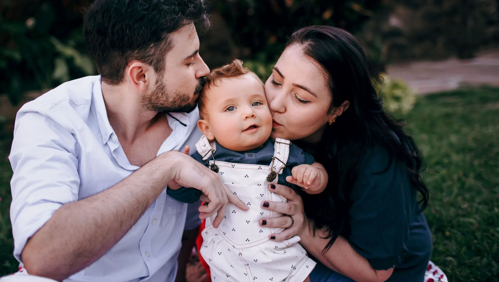 Cherished family moment outdoors with parents lovingly embracing their baby.