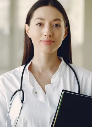 Crop smiling young ethnic female doctor in medical uniform with stethoscope and notebook standing in modern medical room with panoramic window