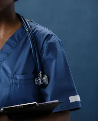 Close-up of a healthcare professional in blue scrubs with a stethoscope and clipboard.