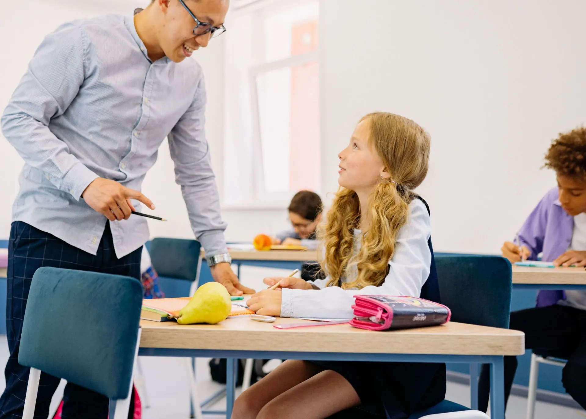 A male teacher interacting with diverse students in a bright classroom setting, promoting active learning.