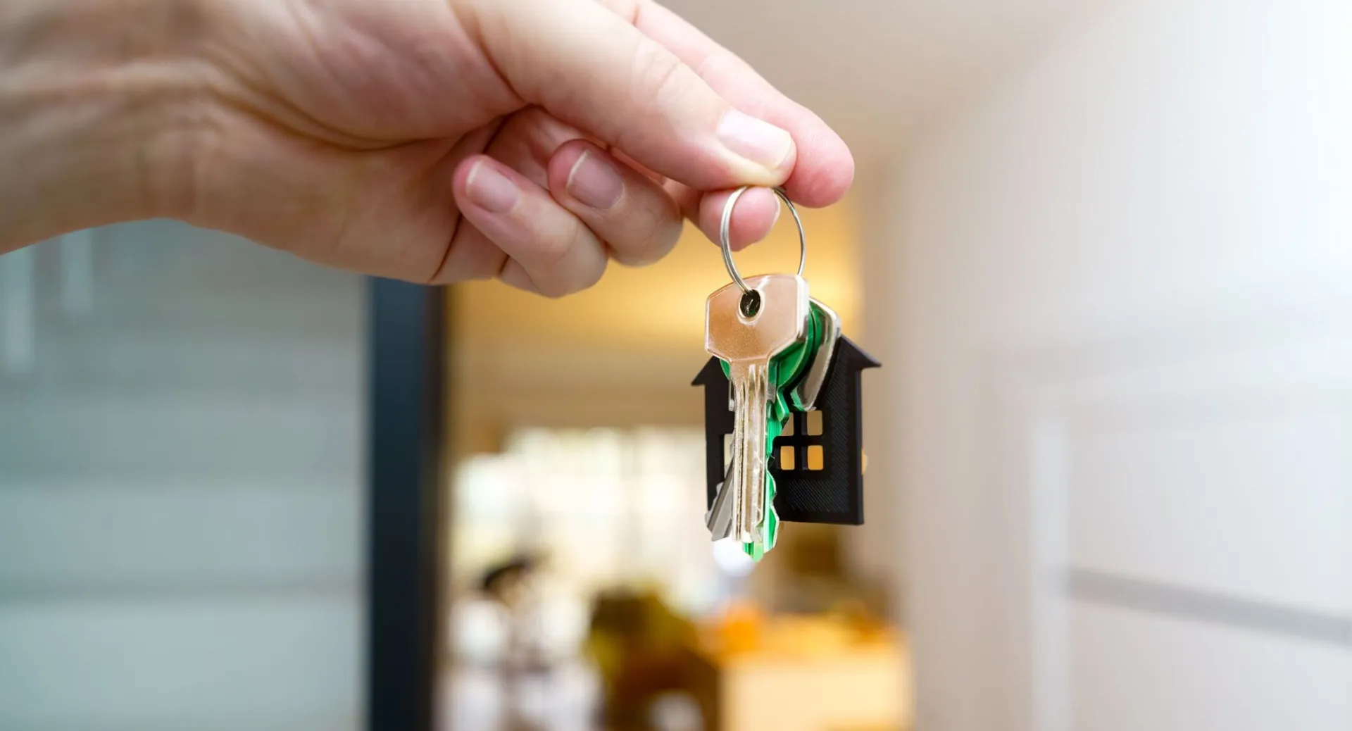 A hand holding house keys inside a modern apartment, symbolizing new property ownership or rental.