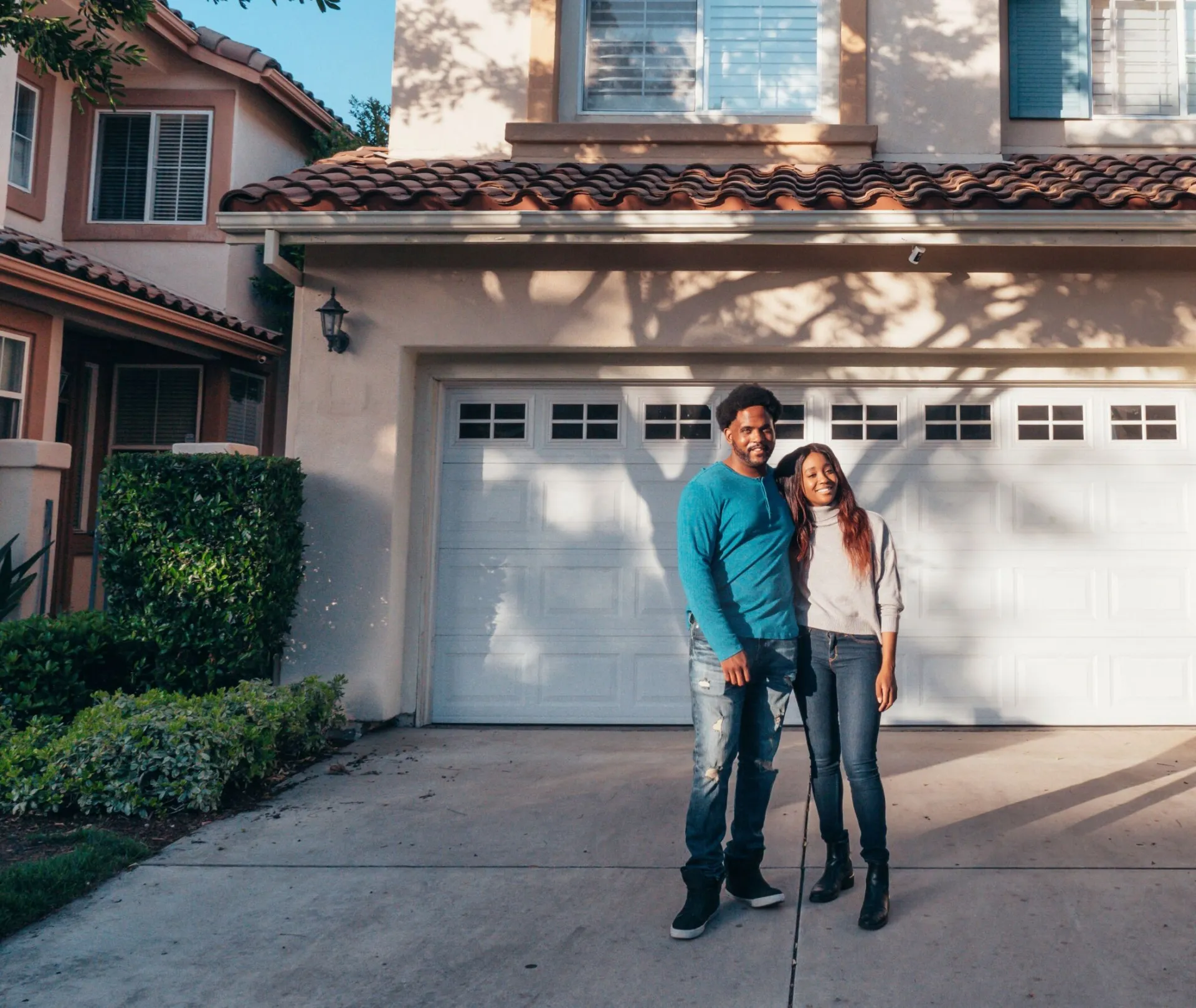 A joyous couple stands together in front of their newly purchased house, symbolizing new beginnings.