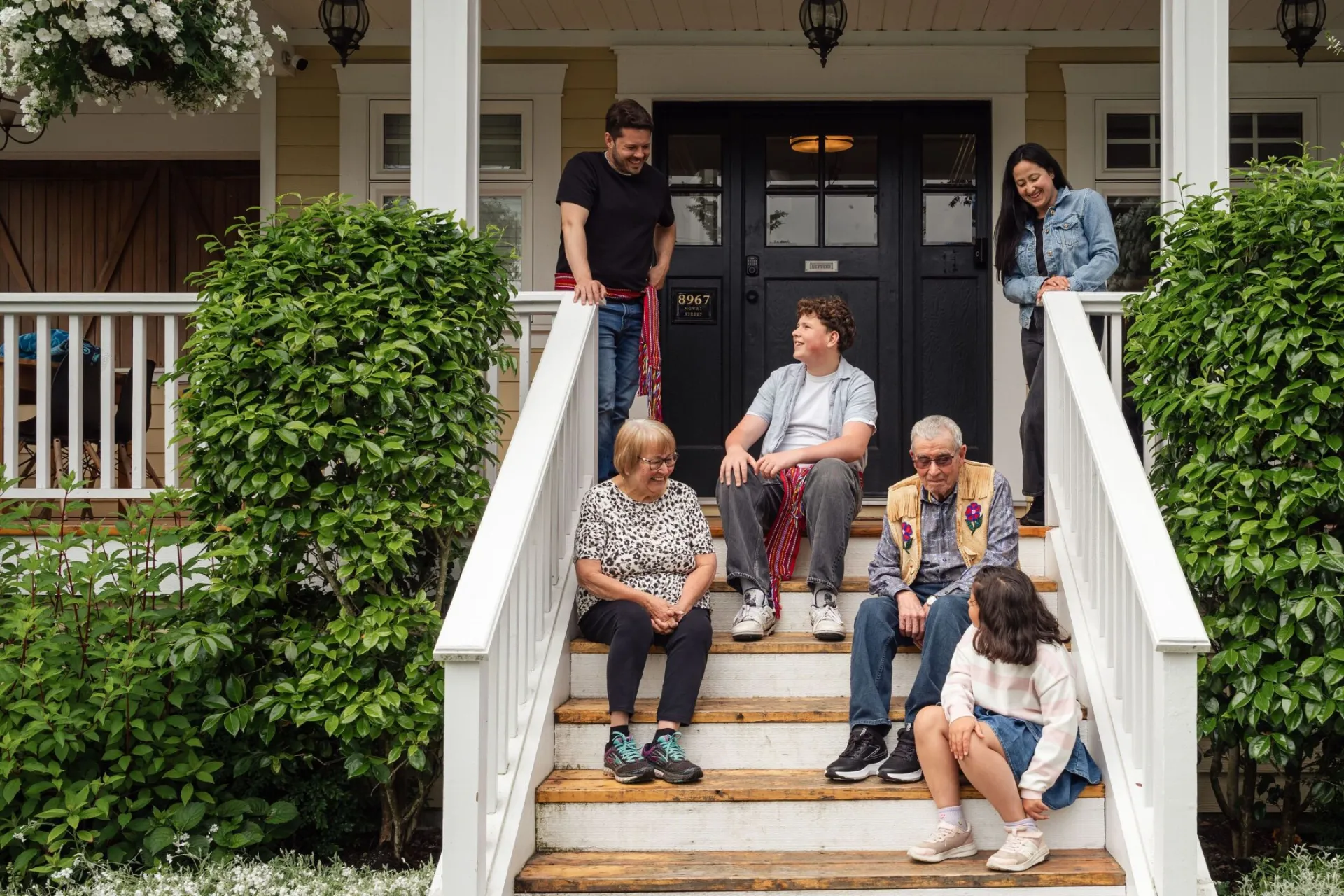 Multigenerational family enjoying a moment on porch steps surrounded by greenery.