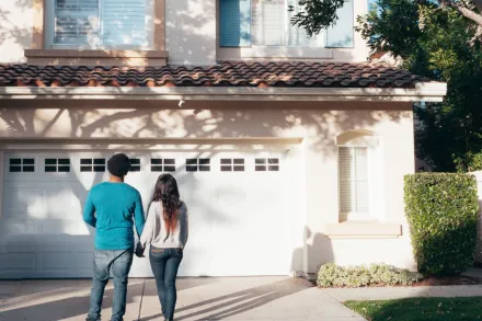 A couple stands hand in hand, admiring their new house and life ahead.