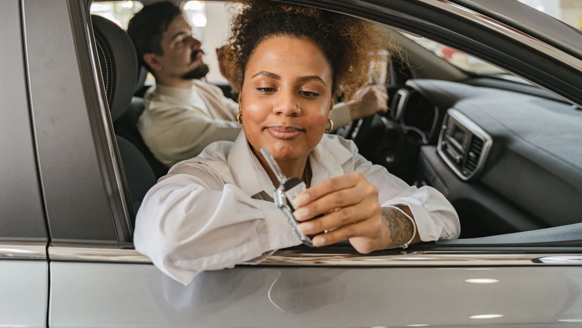 A man and woman in a car, showing car keys, symbolizing freedom and driving adventure.