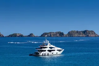 Luxury yacht in serene blue sea with scenic Spanish islands in background.