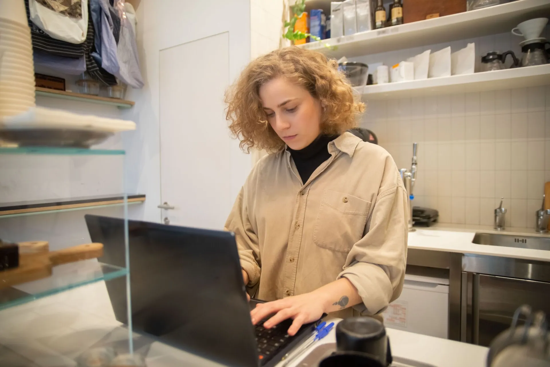 Caucasian woman focused on typing at a laptop in a boutique cafe setting.