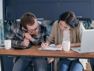 Couple reviewing financial documents together at a kitchen table with a laptop and calculator.