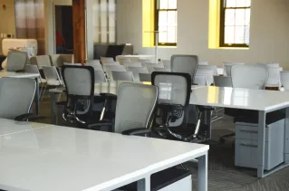 Spacious open office workspace with desks, chairs, and natural lighting.